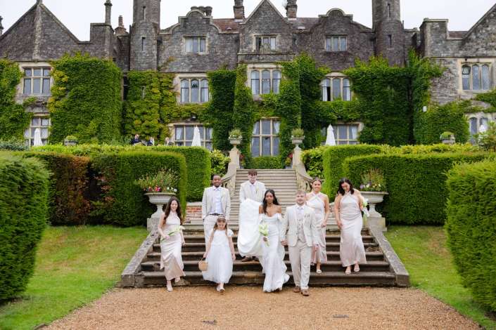 bridal party descending mansion steps A wedding party in pale dresses and light suits descends a grand stone staircase in front of an ivy-covered historic mansion.