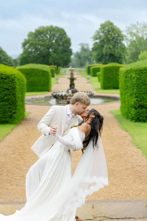 romantic garden wedding kiss A bride and groom kiss as he dips her on a gravel garden path, with a fountain and neatly trimmed hedges in the background.