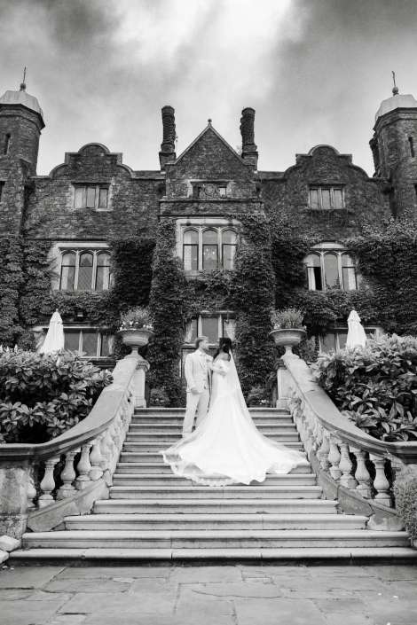 bride and groom on ivy staircase Bride and groom in wedding attire stand on a grand stone staircase before an ivy-covered, castle-like mansion.