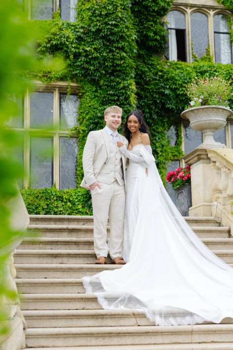 bride and groom on stairs A bride and groom pose on stone steps in front of a ivy-covered historic building, the bride in a long white wedding gown with a flowing train.