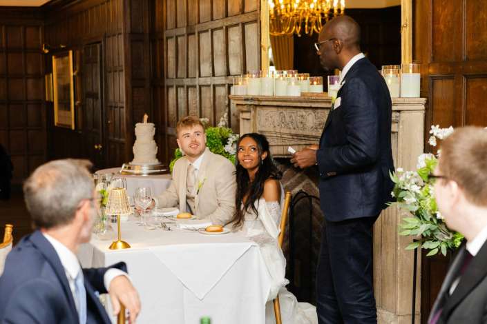wedding speech at reception Bride and groom listen to a standing guest giving a toast at their candlelit, wood-paneled wedding reception.