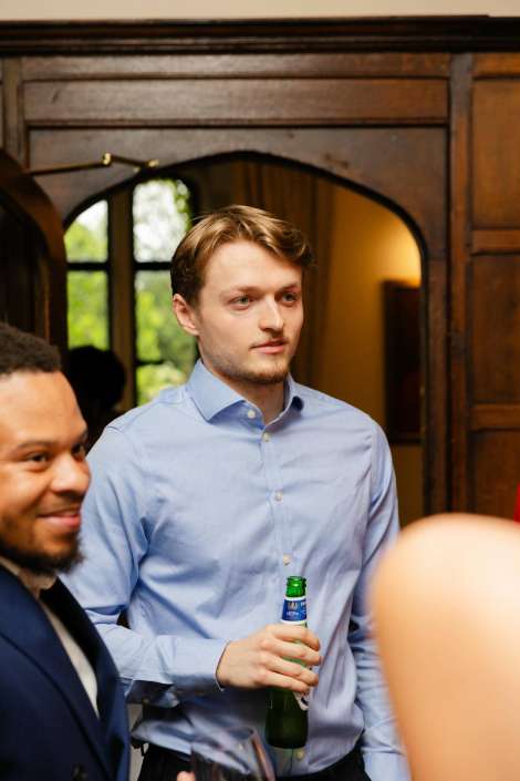 young man holding beer Young man in a light blue button-down shirt holding a beer bottle at a social gathering.