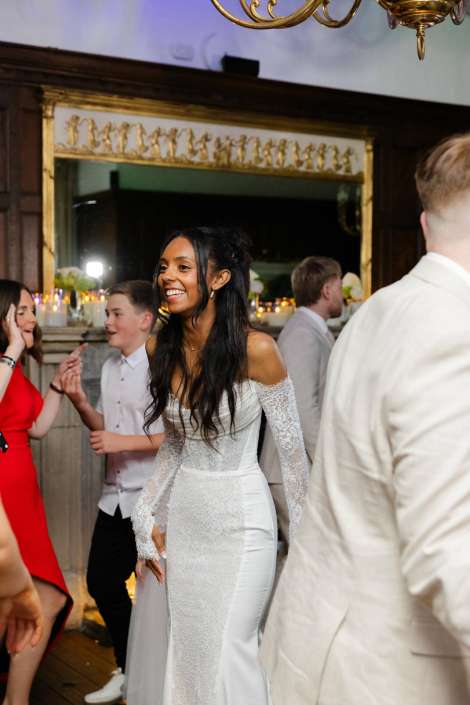 bride dancing at reception Smiling bride in an off-the-shoulder lace wedding gown dancing at a reception with guests.