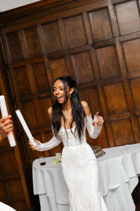 bride celebrating with candles Bride in a white lace wedding dress smiles and gestures indoors beside a table with candles.