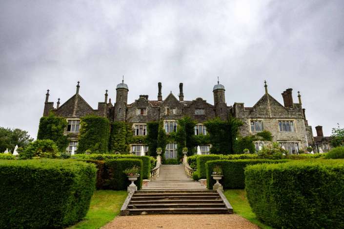 ivy covered manor house A historic stone manor covered in ivy with multiple towers and a grand central staircase flanked by formal, clipped hedges.