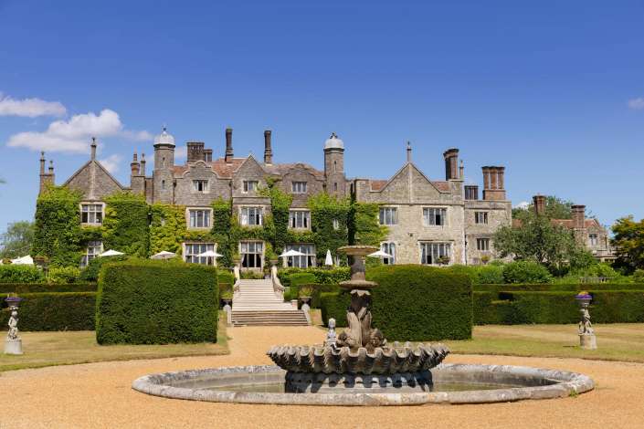 historic manor with fountain A historic stone manor with ivy-covered walls, tall chimneys, and a circular fountain in the formal front garden.