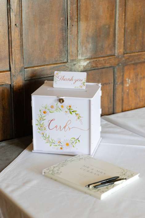 floral card box display A white wedding card box with a floral wreath and the word “Cards” sits on a white table, topped with a small “Thank you” card.