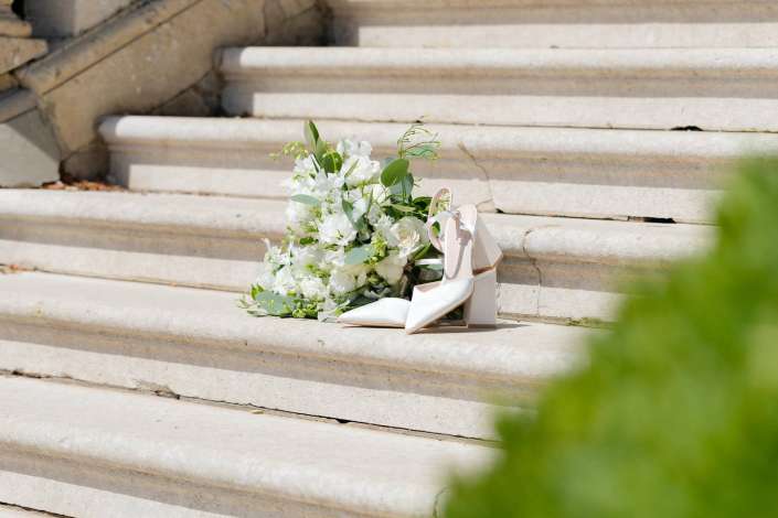 bridal bouquet on steps A white bridal bouquet with greenery and white high-heeled shoes resting on stone steps.