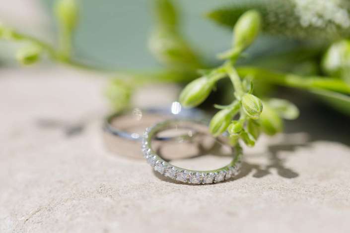 diamond ring closeup Diamond-encrusted eternity ring resting on a light stone surface with blurred green buds and flowers in the background.