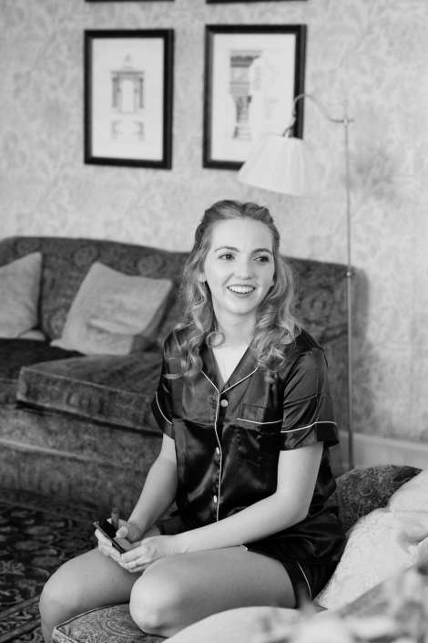 smiling woman in satin pajamas Smiling woman with wavy hair in satin pajamas sits on a sofa in a living room, holding a small makeup item.