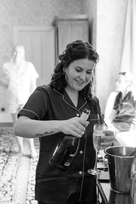 bridal shower champagne pour A smiling woman in dark pajamas pours champagne into a flute at a party, with an ice bucket nearby.