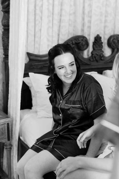 smiling woman in satin pajamas Smiling woman in satin pajamas sits on a bed in a bedroom with an ornate carved headboard.