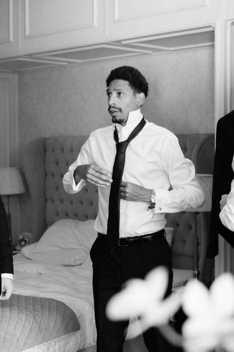 man adjusting his tie A man in a white dress shirt and black tie stands in a bedroom, adjusting his necktie.