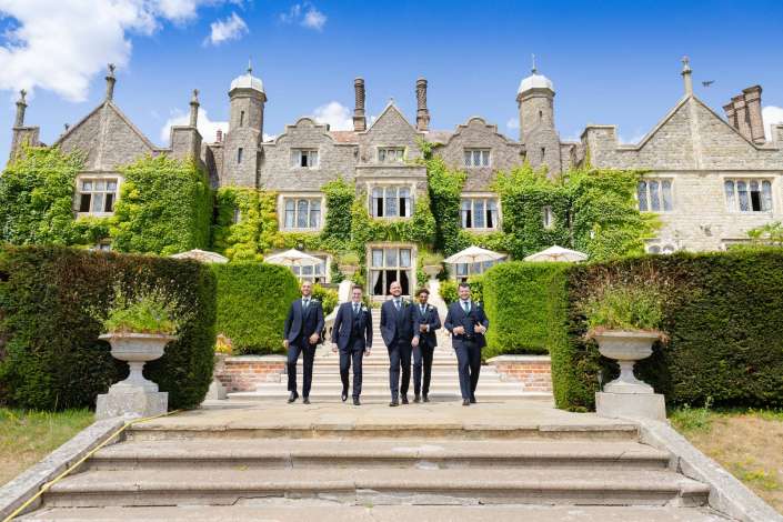 wedding party at historic manor Group of men in navy suits walking down stone steps in front of an ivy-covered historic mansion.