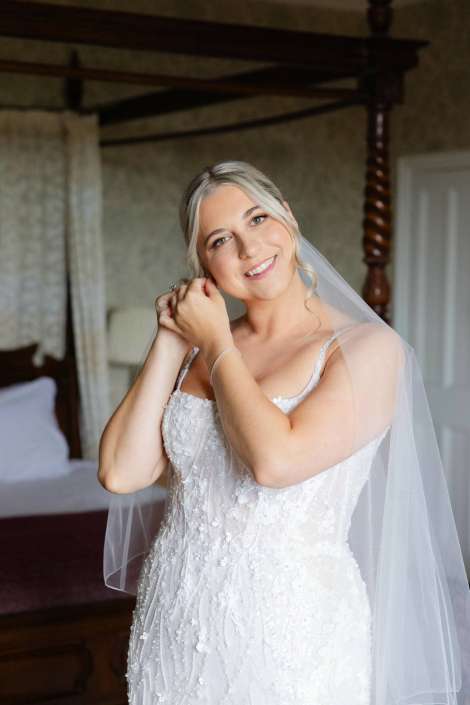 bride putting on earrings Smiling bride in a lace wedding gown with a veil adjusts her earring.