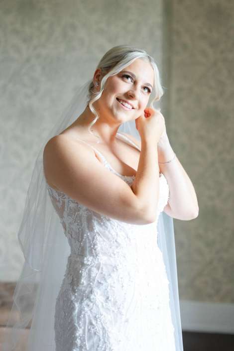 bride in lace wedding dress Smiling bride in a lace white wedding gown with a veil, adjusting her earring.