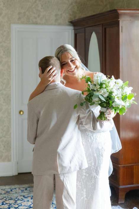 bride embracing groom with bouquet Bride in a white lace wedding gown smiles as she embraces a partner in a light suit, holding a bouquet of white flowers and greenery.