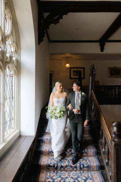 bride and groom descend staircase Bride in a white wedding gown and veil walks down a patterned carpeted staircase with her groom in a dark suit inside a historic building.