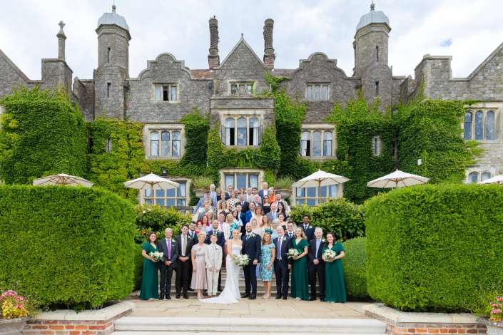 ivy covered castle wedding Bride and groom stand with a large wedding party on the stone steps of an ivy-covered turreted manor.