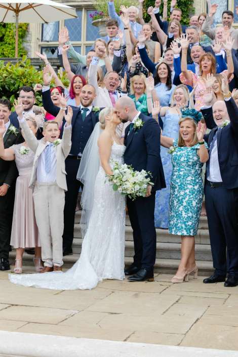 bride and groom kiss with guests Bride and groom kiss while wedding guests cheer and raise their hands on the steps behind them.