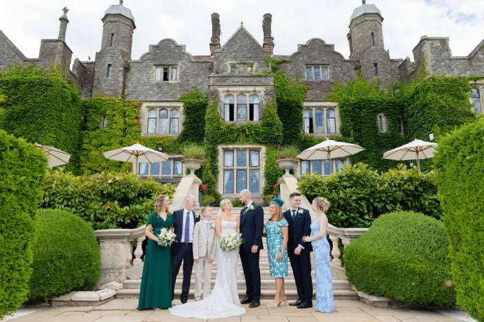 ivy mansion wedding party Bride and groom with bridesmaids and groomsmen pose on stone steps in front of an ivy-covered castle-like manor with tall turrets.