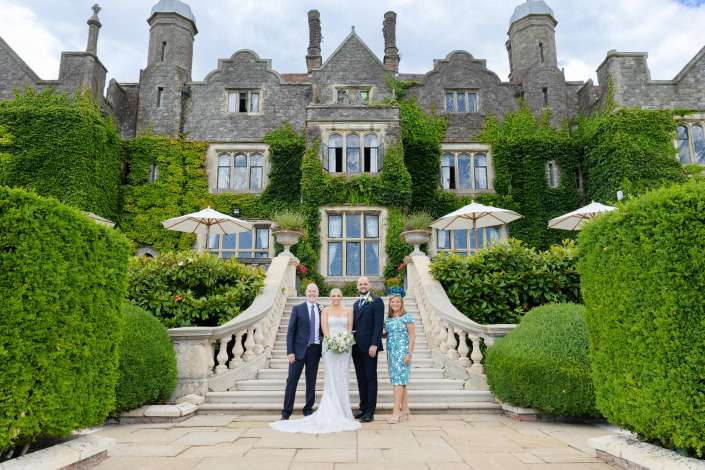 ivy covered manor wedding Bride and groom pose with two guests on a grand stone staircase in front of an ivy-covered historic manor.