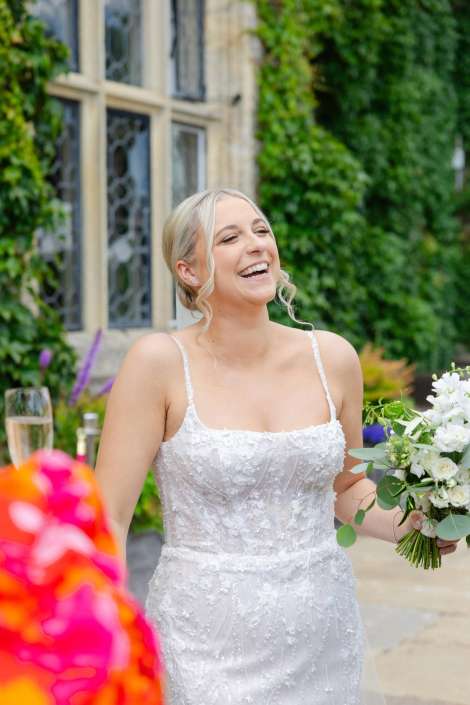 joyful bride in white A smiling bride in a white lace wedding dress holds a bouquet of white flowers outdoors.