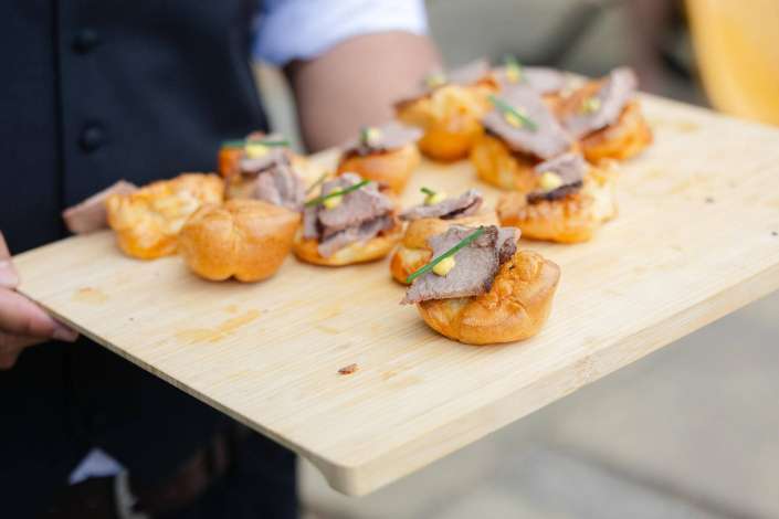 roast beef crostini bites Assorted beef crostini bites topped with roast beef, mustard and chives on a wooden cutting board.
