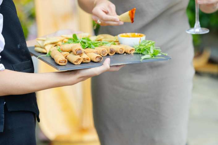 assorted spring rolls platter Tray of fried spring rolls and chips with greens and a small dipping sauce, being served.