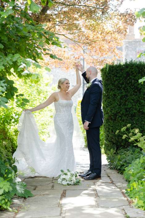 sunlit garden wedding dance Bride and groom dancing on a sunlit garden path, she lifts her wedding dress as he holds her hand.