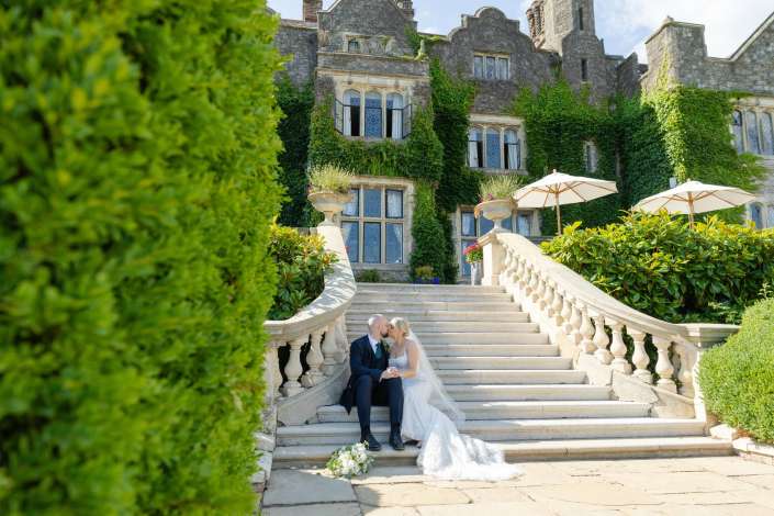 bride and groom on grand staircase Bride and groom share a kiss on a grand stone staircase in front of an ivy-covered, castle-like building.