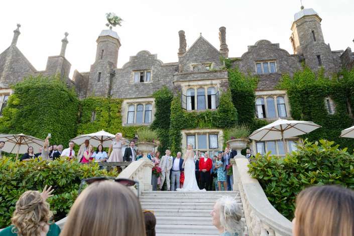 castle wedding party on steps Bride and wedding party pose on the grand stone staircase of an ivy-covered castle-like mansion.
