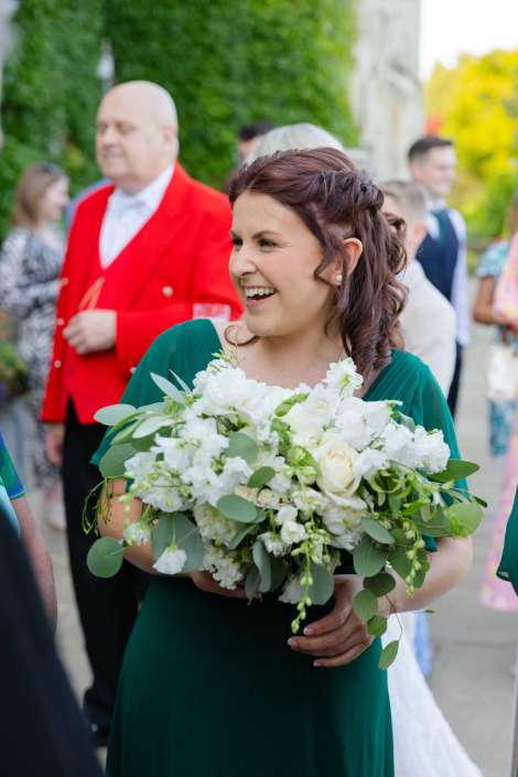 smiling woman with white bouquet Smiling woman in a green dress holding a large white floral bouquet outdoors.
