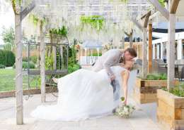 Bride and groom share a kiss as the groom dips the bride beneath a flowering wooden pergola. Photo by Louisa Dettmer Wedding Photography, Kent Wedding Photographer