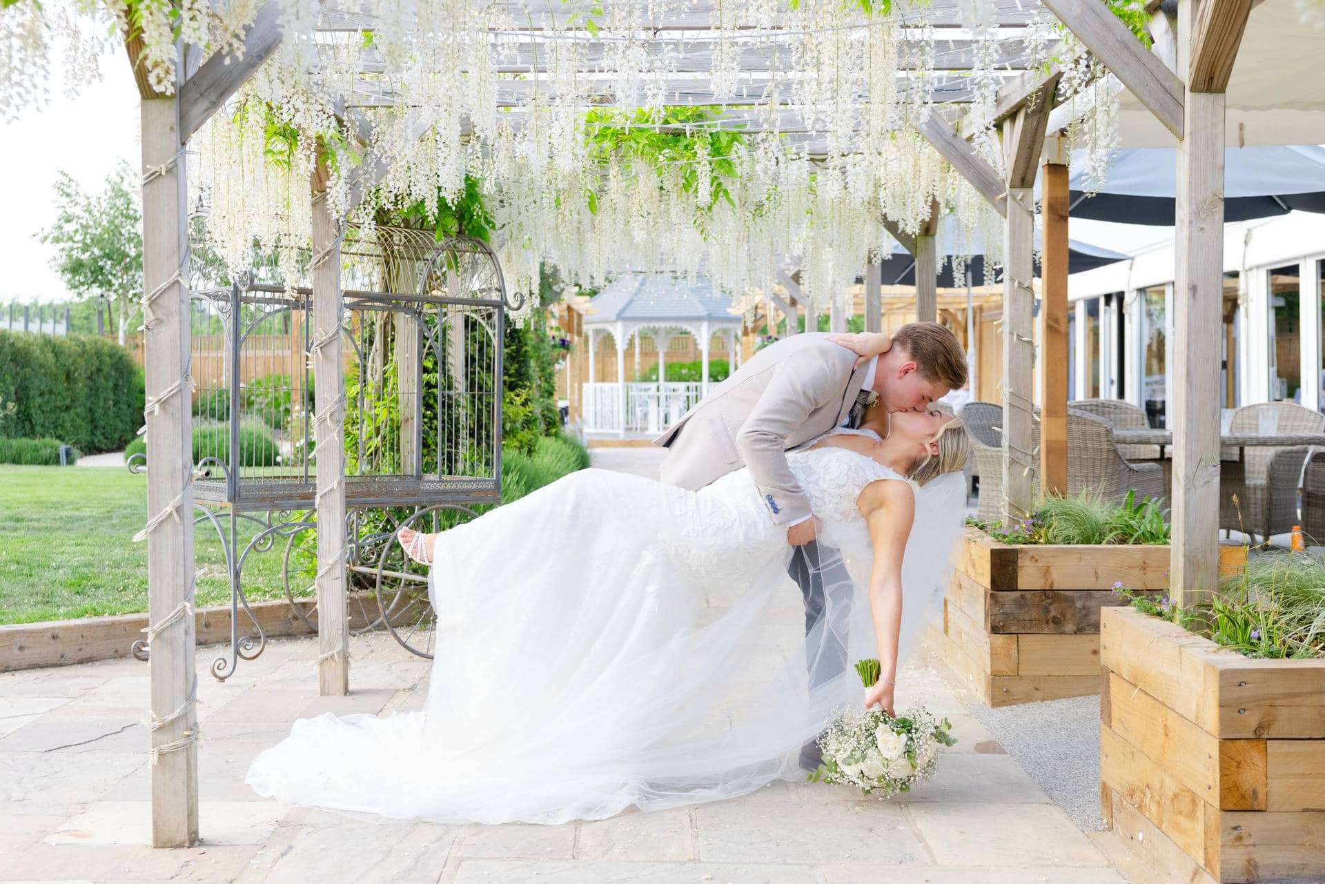 gemma & sam, the barnyard, louisa dettmer photography Bride and groom share a kiss as the groom dips the bride beneath a flowering wooden pergola. Photo by Louisa Dettmer Wedding Photography, Kent Wedding Photographer